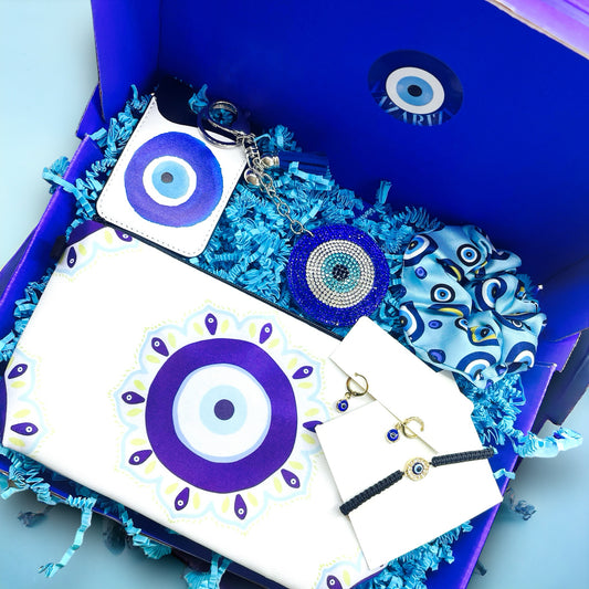 Boze Oog Cadeaubox Charm met Nazar Safe pasjeshouder, donkerblauwe Nazar Eye sleutelhanger, Nazar Aqua scrunchie, Nazar Golden oorbellen, Nazar Hypnotic Boze Oog armband, en Nazar Sunshine makeup-tas/toilettas. Een luxe geschenkset vol met stijlvolle en betekenisvolle accessoires, perfect voor een boodschap van liefde en geluk.